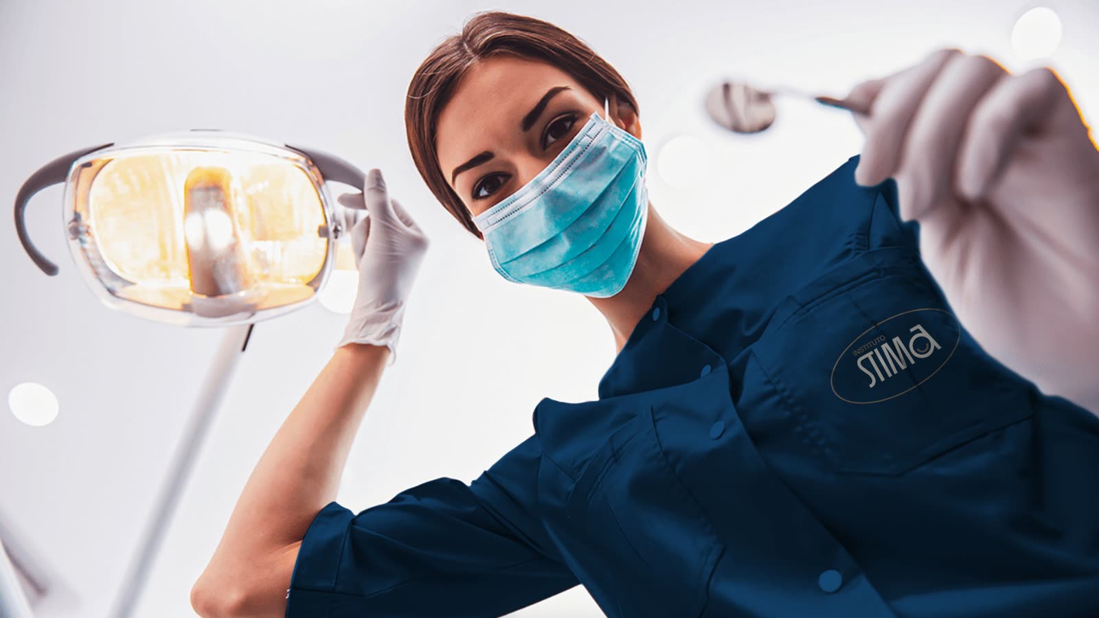 A dentist in a navy STIMA uniform holding a dental mirror